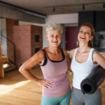 a warm wood yoga studio has a middle age and older woman in it who just completed a yoga session. they have on tight fitting yoga clothes and are happy about peptides for women that keep them performing how they did their whole life long.