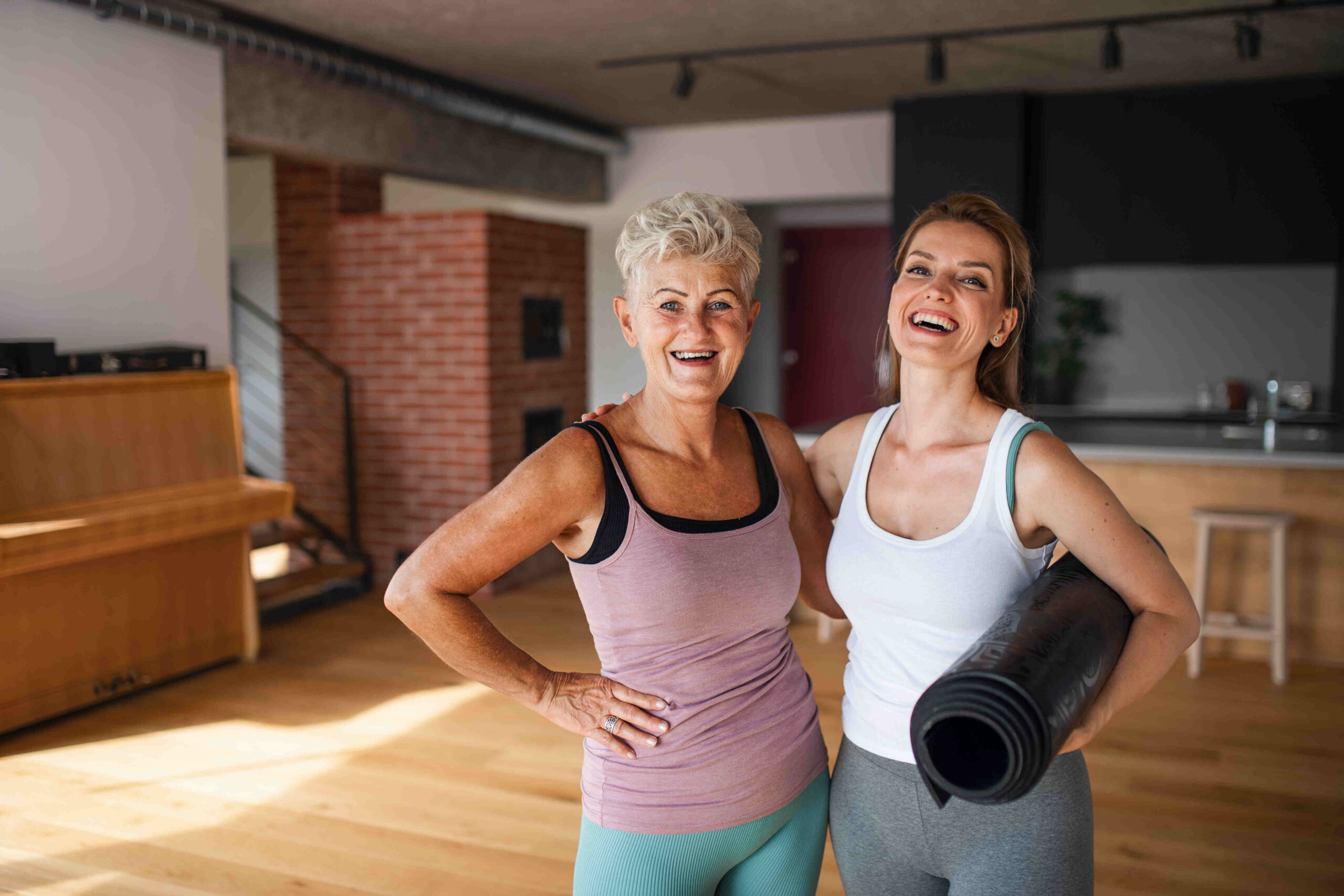 a warm wood yoga studio has a middle age and older woman in it who just completed a yoga session. they have on tight fitting yoga clothes and are happy about peptides for women that keep them performing how they did their whole life long.